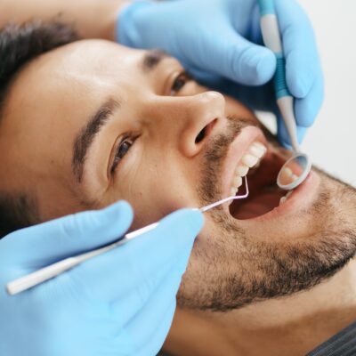 smiling-young-man-sitting-in-dentist-chair-while-doctor-examining-his-teeth-min-scaled-1